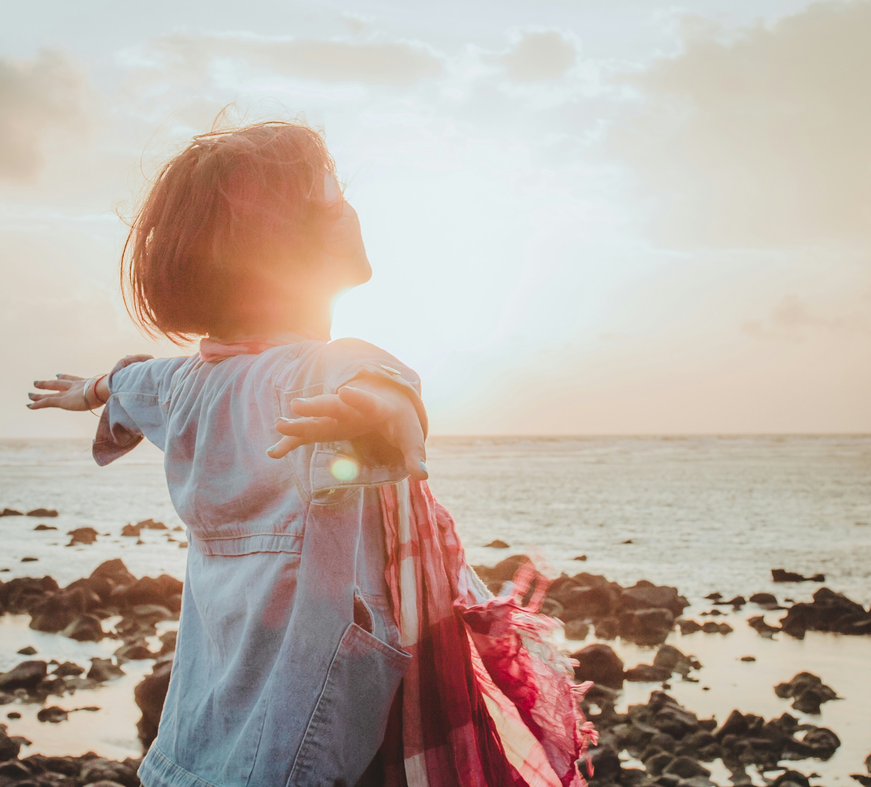 Woman standing at the shore at sunrise with arms open